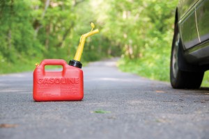 A red plastic gas can sitting in the middle of a country road next to a car.